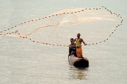 Two people on a boat cast a net for fish in Lake Malawi