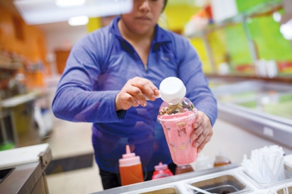 A woman pours dry toppings onto shaved ice