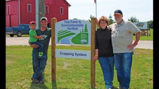 The Stover family stands in front of a sign signifying their farm, Berrien Springs, participates in the MAEAP program.
