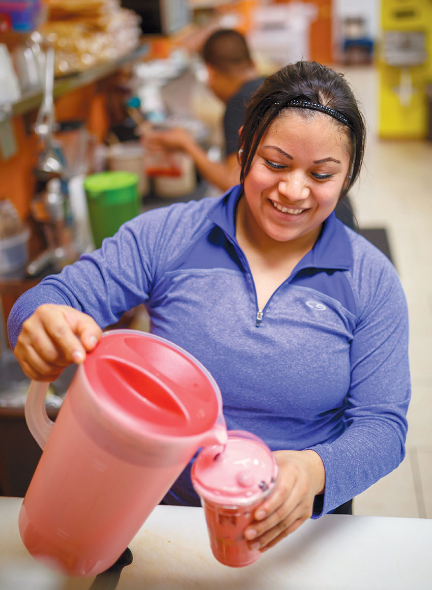 A woman pours wet toppings onto shaved ice.